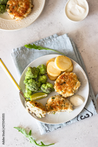 Delicious cutlets (fish or meat) with broccoli, potatoes and sauce on a plate. Light grey stone background. 