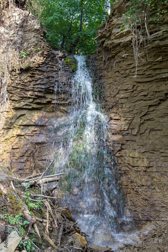 Waterfall in the forest at summer day. Fallen stones, tree brenches and old roots photo