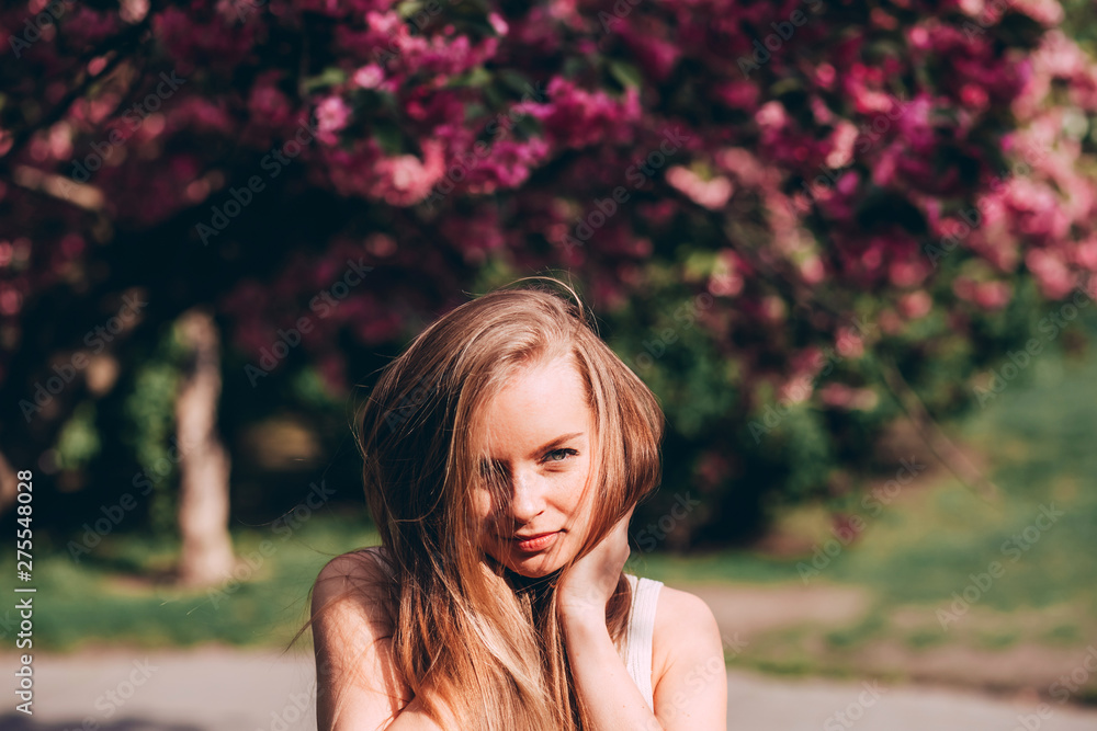 Fototapeta premium romantic portrait of charming blonde on the background of a blooming garden. Tree with pink flowers. Beauty blonde woman with long hair outdoors. Cherry blossoms. Close up portrait. Sakura