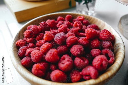 Ripe raspberries in a wooden plate on the table