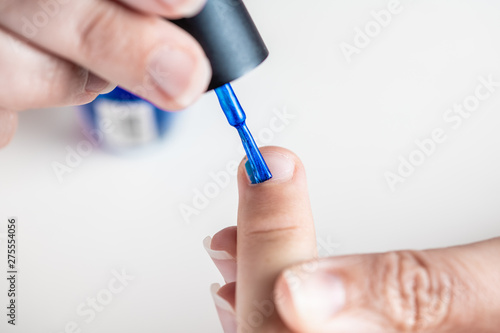 A mother paints her young girl s hands with blue and pink nailpolish  viewed against an isolated white background