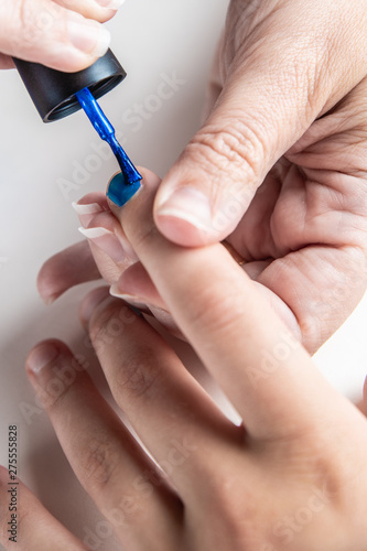 A mother paints her young girl's hands with blue and pink nailpolish, viewed against an isolated white background