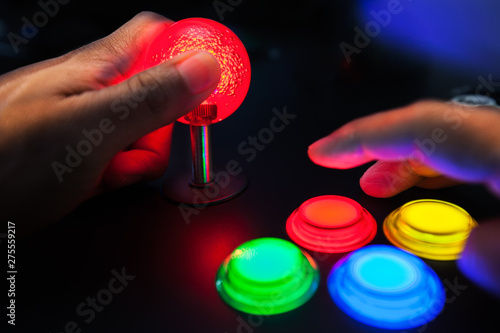 A red lighted arcade joystick and four button layout push buttons being played by a video gamer on a retro arcade machine.