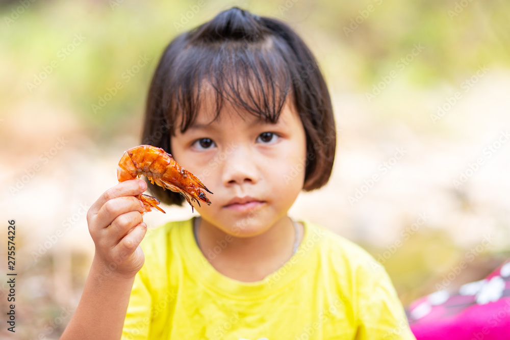 Little Asian girl holding a piece of grilled shrimps Little Asian girl holding a piece of grilled shrimps