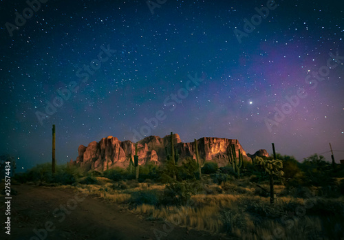 The desert wilderness east of Phoenix, Arizona photographed under clear starry desert skies that seem to glow with color. Desert plants and Saguaro cactus grow around the Superstition mountains 