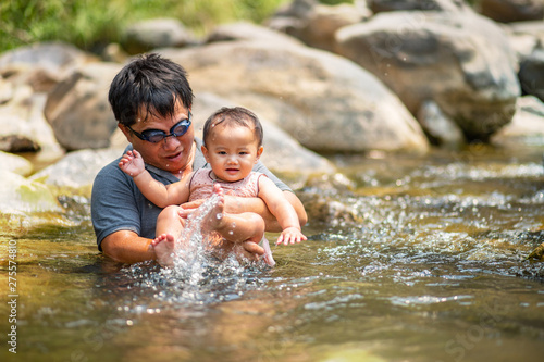 Asian man wearing goggles holding his baby girl in water