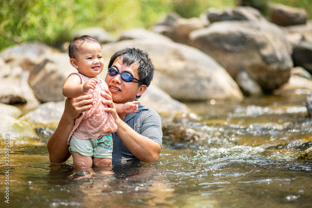 Fototapeta premium Asian man wearing goggles holding his baby girl in water