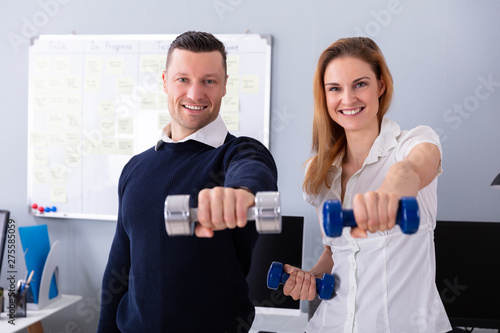 Businesspeople Exercising With Dumbbells In Office