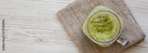 Green celery smoothie in a glass jar over white wooden background. Overhead, flat lay, from above. Space for text.