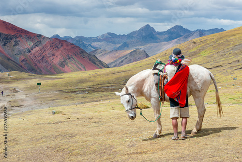 Man dressed in traditional clothing with a horse in Rainbow Mountain, near Cusco, Peru