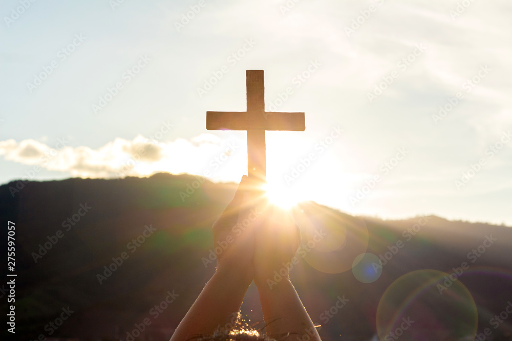 human hands praying to the GOD while holding a crucifix symbol with bright sunbeam on the sky