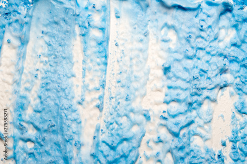 Blue paint spilled over white background. Textured colored foam surface with grainy shimmer effect. © golubovy