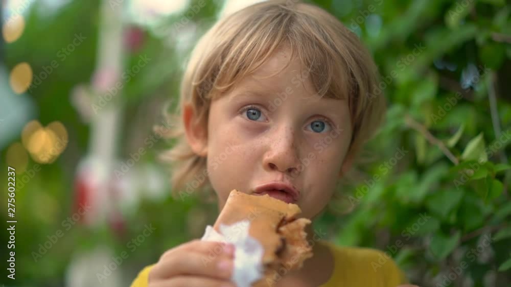 Closeup shot of a little boy eating a tasty pancake on a street market. Street food concept. Closeup shot of a little boy eating a tasty pancake on a street market. Street food concept.