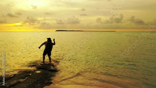 A silhouette of a woman picking up something is staying on a rock in shallo water. Looking at the sea, which is lit by the golden sunlight. In Bali. Truck left photo