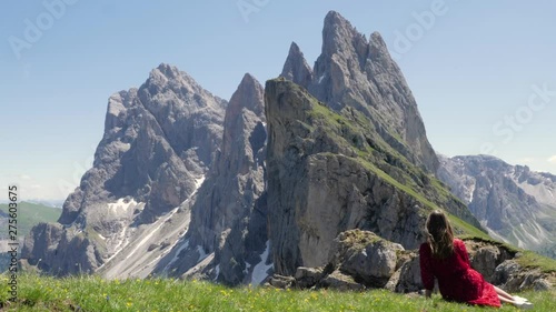 Wallpaper Mural Slow motion shot of young woman in red dress sitting on grass looking at the slopes of Seceda in the Dolomites, Italy in the summer - handheld camera moving up Torontodigital.ca