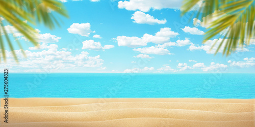 Summer beach with palm leaves. Sand, sea and blue sky with clouds. Copy space in the middle for promo text or logo. Summer travel concept.