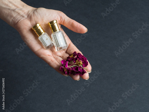 Concentrated perfume in a mini bottle in the hand with floral petals on the black background photo