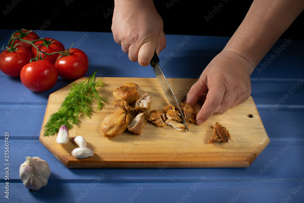 Baked chicken on a board on a blue wooden background with dill, tomatoes, garlic, with a knife and fork in hand.