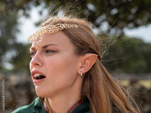 Close-up of blonde girl with blue eyes and elf ears wearing a green cape photo