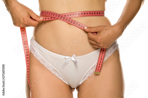 Woman measures her waist with metering tape on white background