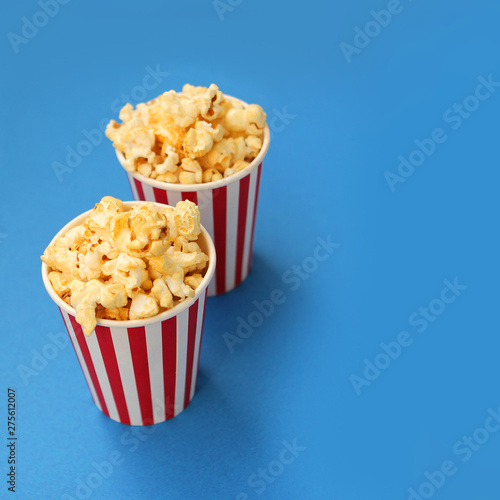 two striped white and red paper cups with fragrant crispy popcorn stand one after another on a light blue background, copy space, close-up, square