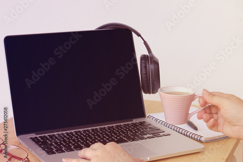 young woman drinks coffee from a small pink cup, sits working at a laptop in an office