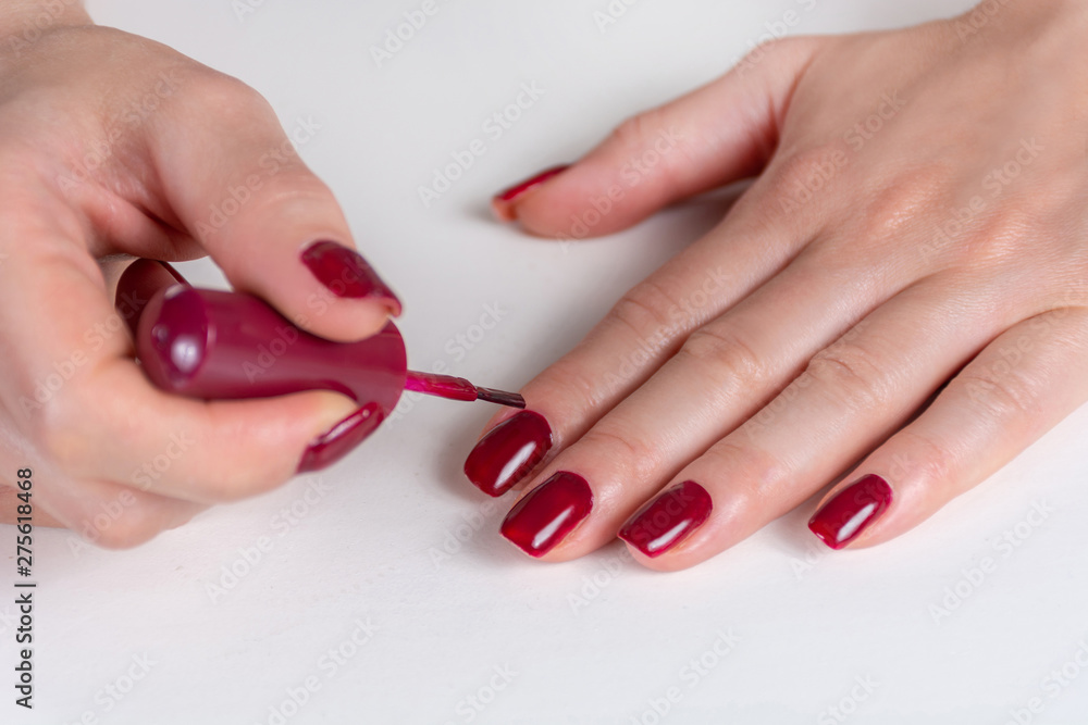 Young woman hand applying dark red nails polish color on her finger with  the brush on white desk. Painting nails and manicure concept. Close up,  selective focus Stock Photo | Adobe Stock