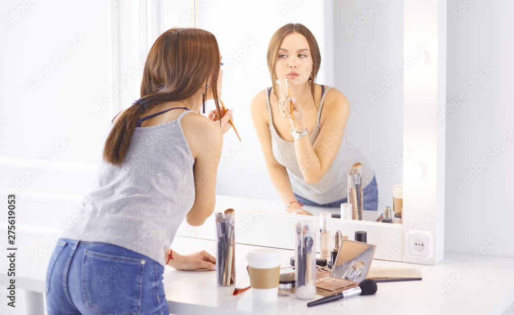 Fototapeta premium Amazing young woman doing her makeup in front of mirror. Portrait of beautiful girl near cosmetic table