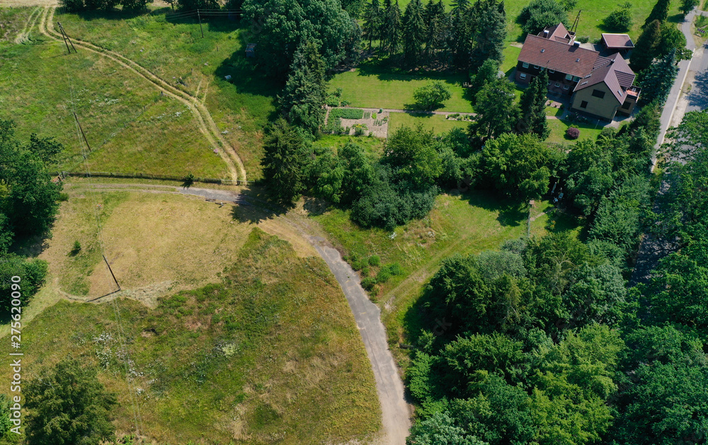 Aerial view of a meadow area with a few houses and a loose stock of bushes and trees.