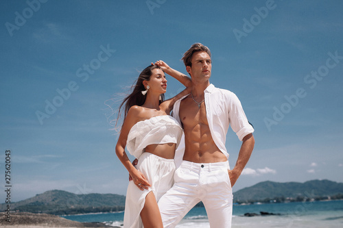 Fashion photo of a beautiful  fitness happy couple in white clothes in love standing  and posing on the beach. Phuket. Thailand