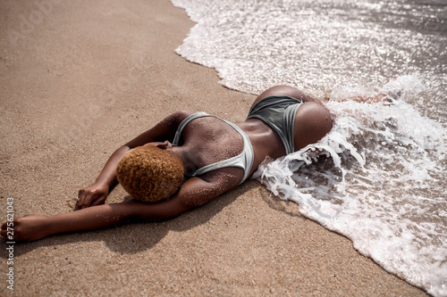 summer photo of sunbathed African American woman lying on summer beach with white sand and big sea waves.Tropical vacation