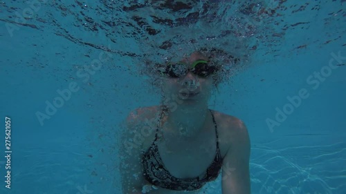 A European woman in a swimsuit and swimming glasses jumps into the pool shooting herself on the action camera, shooting while jumping and under water