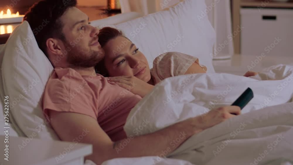 people, family and leisure concept - happy couple watching tv in bed at night at home people, family and leisure concept - happy couple watching tv in bed at night at home