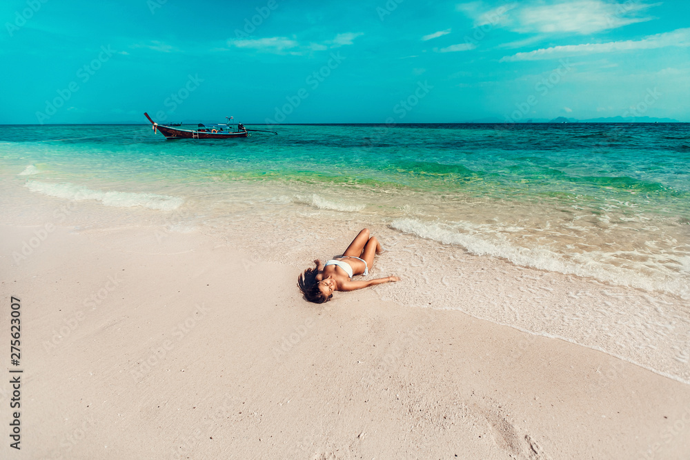 Young and pretty girl model in a bikini sunbathing on the beach resort of the Andaman sea. Boat and blue sea background Young and pretty girl model in a bikini sunbathing on the beach resort of the Andaman sea. Boat and blue sea background