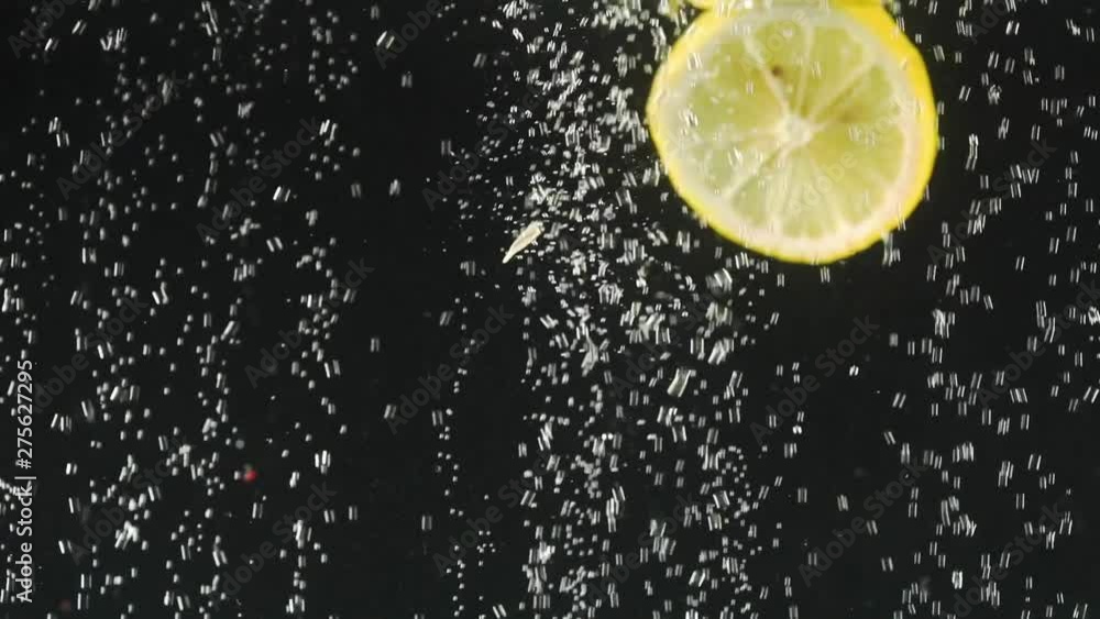 Fresh lemon slices falling into the water on black background. Citrus in water with bubbles. Organic food. Slow motion. Fresh lemon slices falling into the water on black background. Citrus in water with bubbles. Organic food. Slow motion.