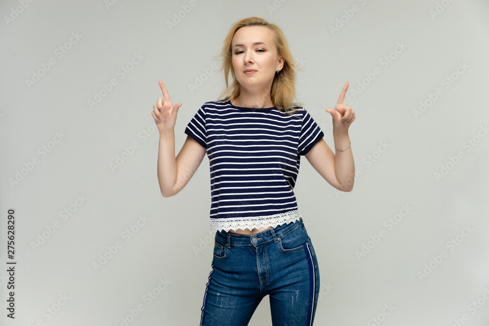 Portrait of a pretty interesting blonde girl on a white background in jeans and a striped blue t-shirt. Standing in front of the camera, smiling, showing hands. Shows a lot of emotions. Portrait of a pretty interesting blonde girl on a white background in jeans and a striped blue t-shirt. Standing in front of the camera, smiling, showing hands. Shows a lot of emotions.