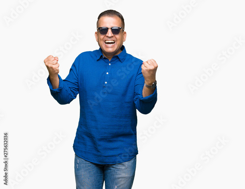 Middle age arab man wearing sunglasses over isolated background celebrating surprised and amazed for success with arms raised and open eyes. Winner concept.