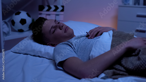 Fotografie Nicotine addicted teen boy falling asleep with cigarette in bed risk of accident