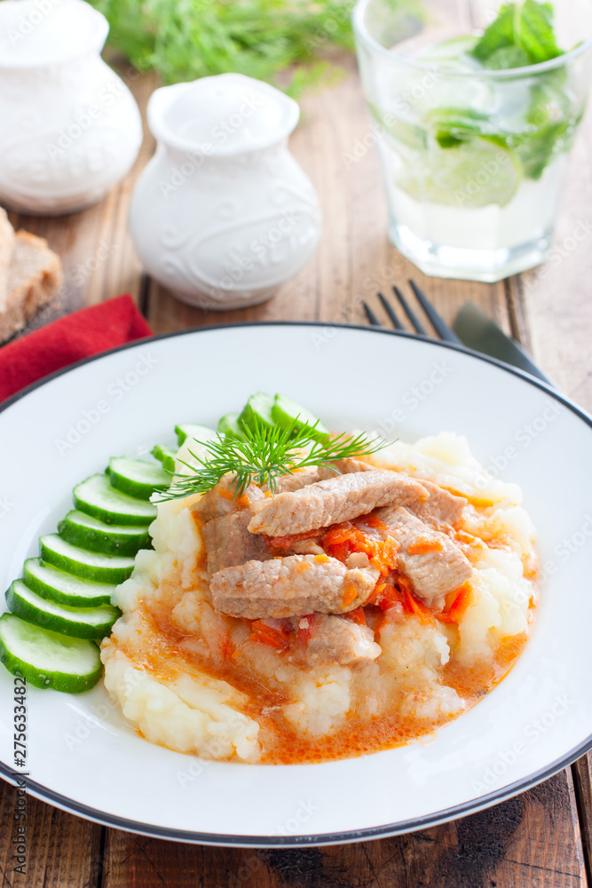 Pork with gravy and mashed potatoes and fresh cucumber on a wooden table, selective focus Pork with gravy and mashed potatoes and fresh cucumber on a wooden table, selective focus