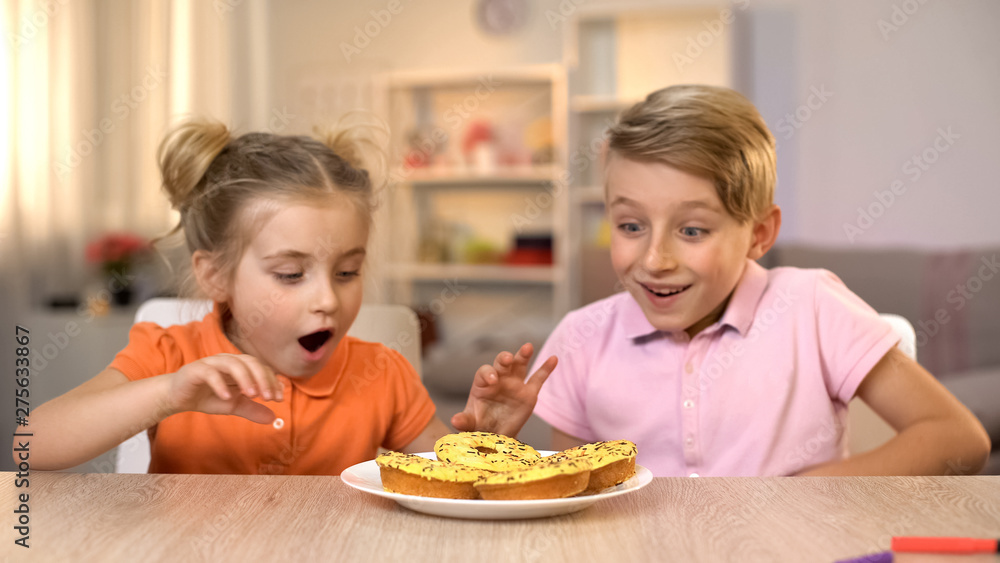 Excited girl and boy looking at yellow donuts, unhealthy but tasty snack, food