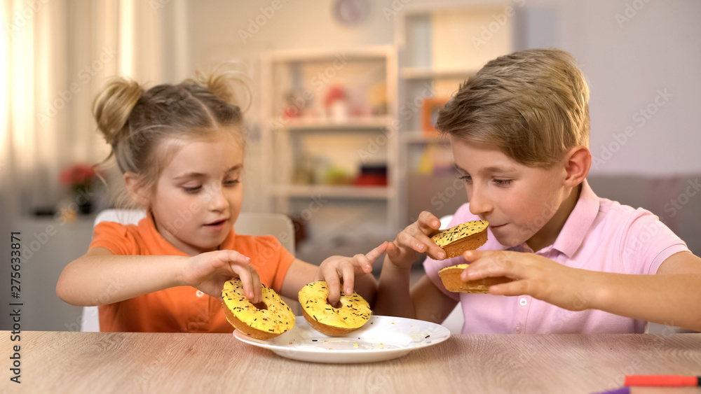 Siblings taking and smelling yellow donuts, unhealthy but tasty snack, food