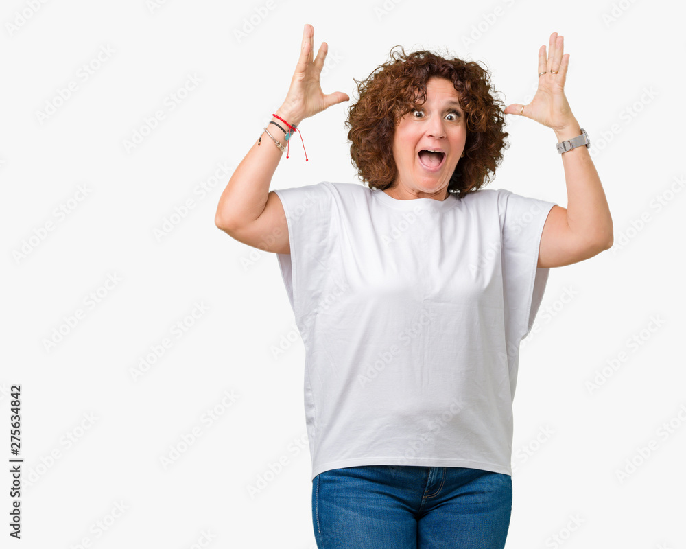 Beautiful middle ager senior woman wearing white t-shirt over isolated background celebrating crazy and amazed for success with arms raised and open eyes screaming excited. Winner concept Beautiful middle ager senior woman wearing white t-shirt over isolated background celebrating crazy and amazed for success with arms raised and open eyes screaming excited. Winner concept