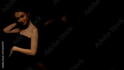 Sexy woman in dress posing for camera, isolated on black background, seduction
