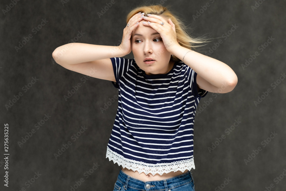 Portrait to the waist of a pretty interesting fashionable blonde girl on a gray background in a striped blue t-shirt. Standing in front of the camera, smiling, showing hands. Shows a lot of emotions. Portrait to the waist of a pretty interesting fashionable blonde girl on a gray background in a striped blue t-shirt. Standing in front of the camera, smiling, showing hands. Shows a lot of emotions.