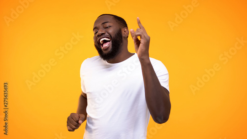 Happy relaxed black man dancing against yellow background, having fun on party photo