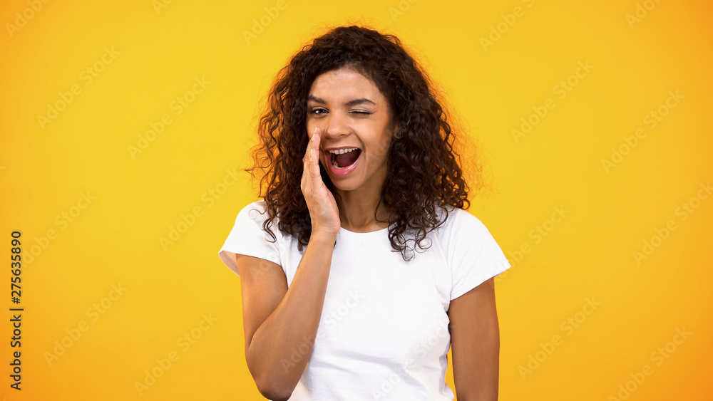 Smiling woman whispering secrets and winking on camera yellow background, rumors Smiling woman whispering secrets and winking on camera yellow background, rumors