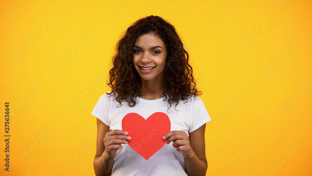 Sincere young woman holding red heart-shaped cutout present on Valentines day Sincere young woman holding red heart-shaped cutout present on Valentines day