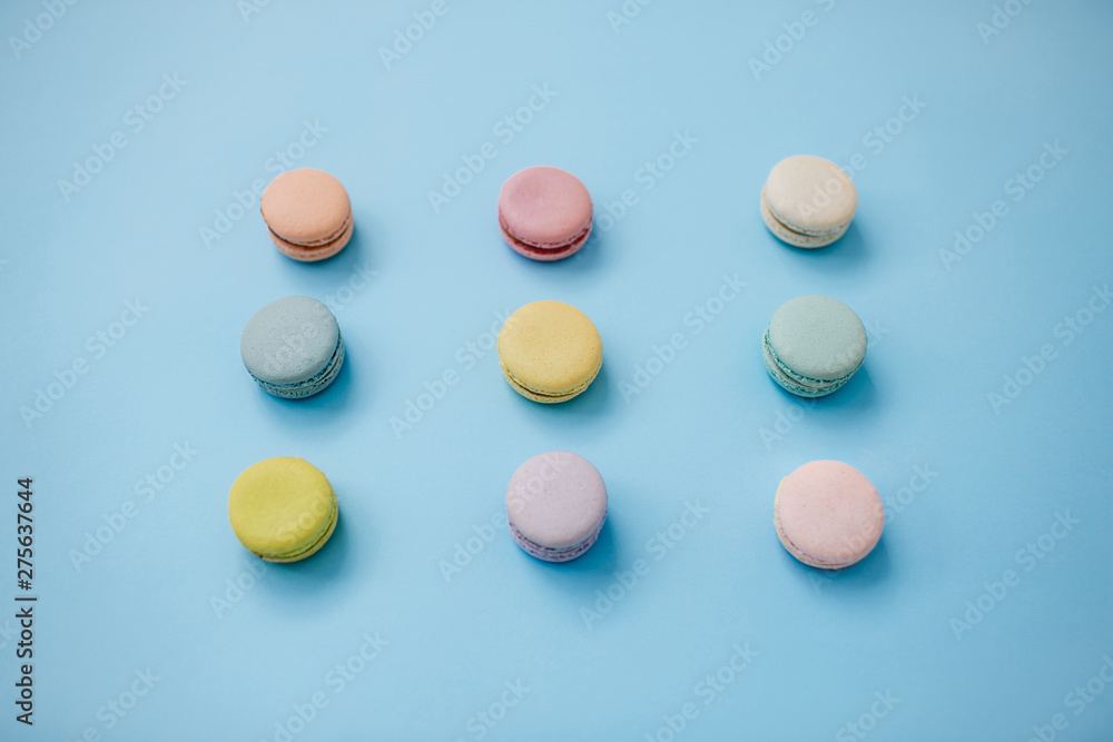 Top view of sweet French macaroon biscuits lying in three lines on pastel blue background. Top view of sweet French macaroon biscuits lying in three lines on pastel blue background.