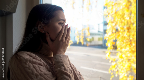 Crying lady looking through window, afraid of going outdoors agoraphobia disease