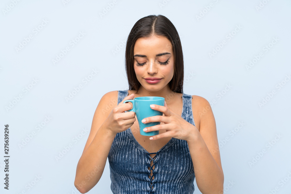 Young woman over isolated blue wall holding hot cup of coffee Young woman over isolated blue wall holding hot cup of coffee